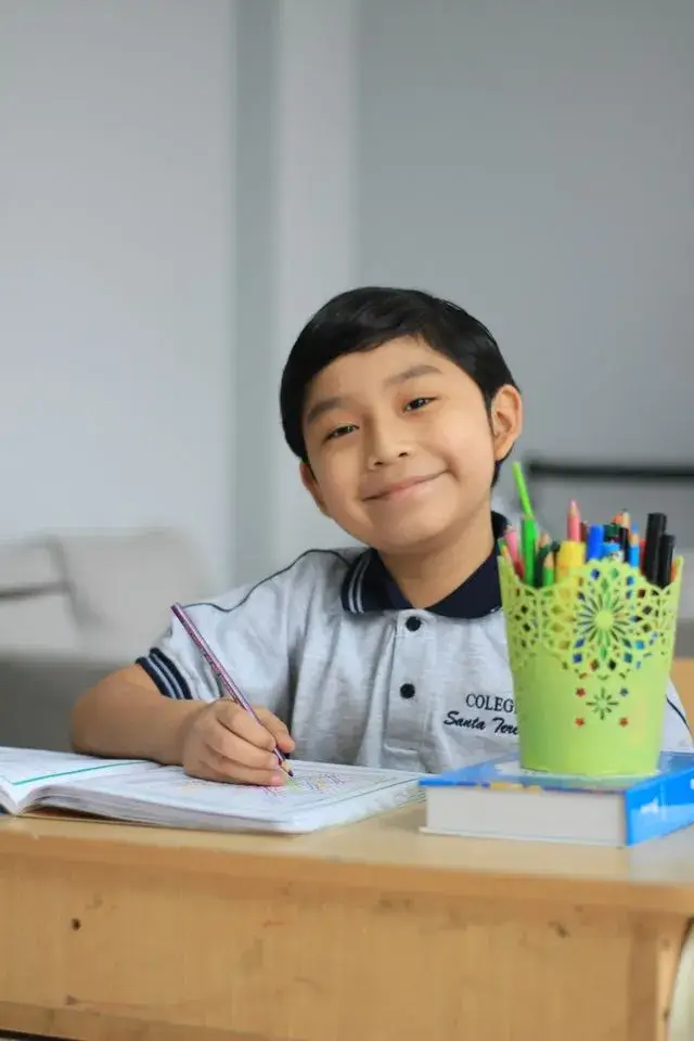 Criança estudando com caderno e materiais escolares.